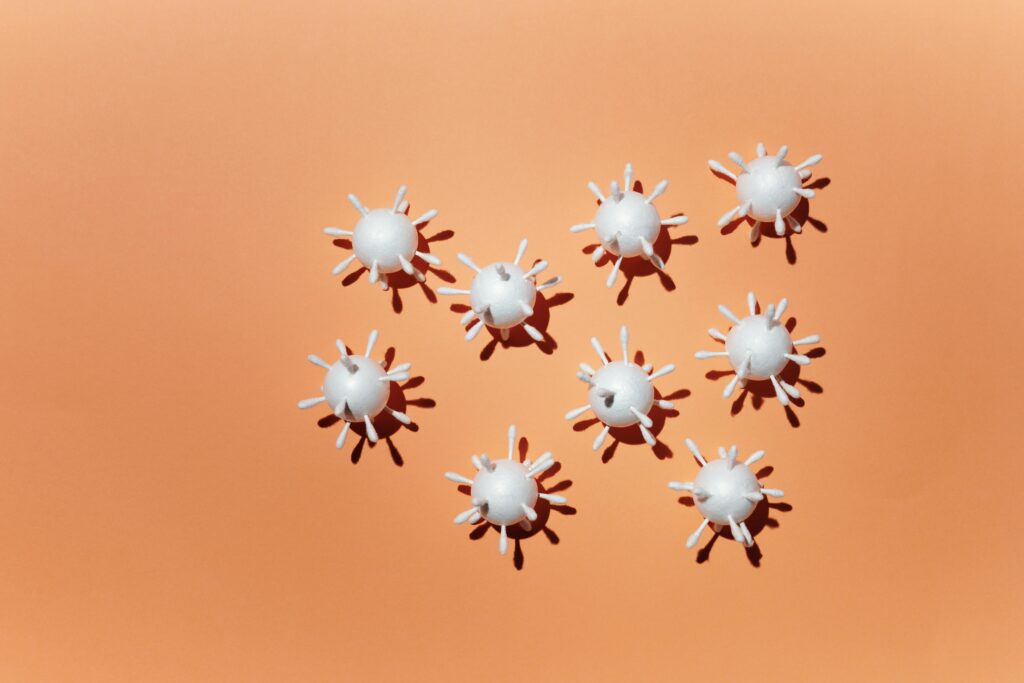 White 3D virus scale models arranged on a peach background, casting shadows.