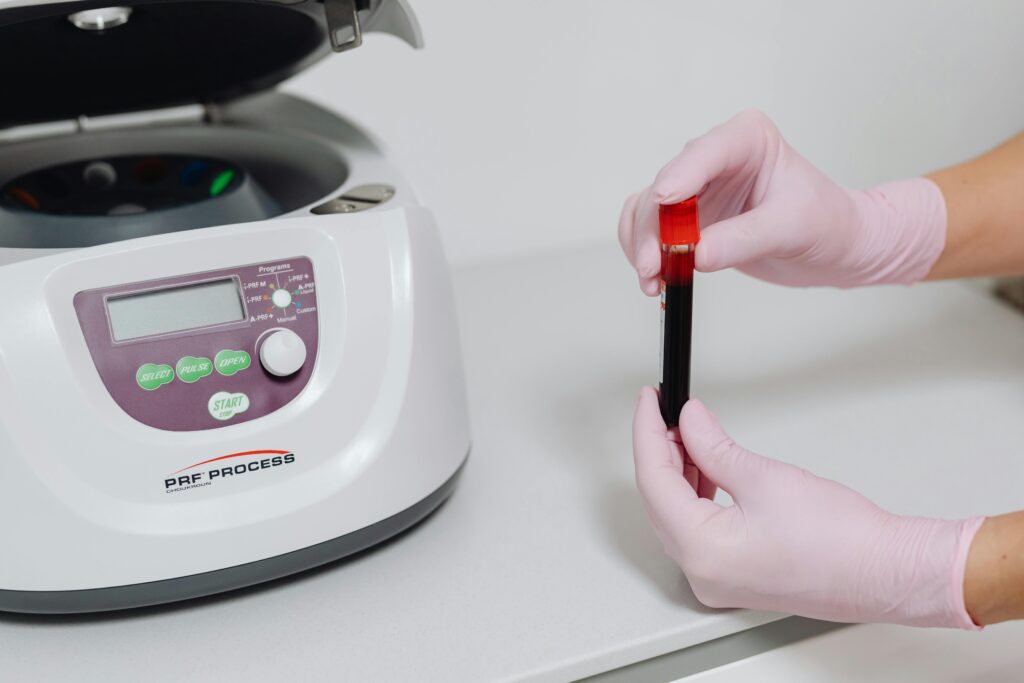 Close-up of hands in gloves holding a blood sample beside a centrifuge.