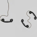 Two vintage black telephone handsets connected by cords on gray background.